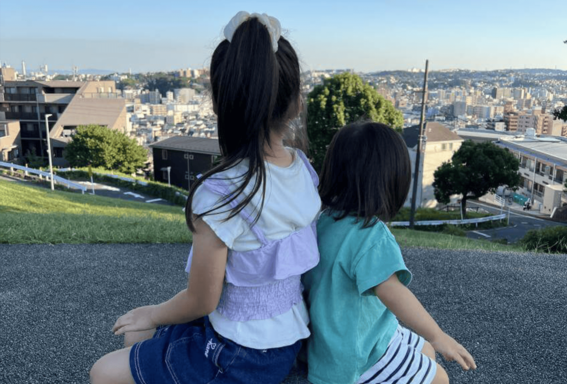 代表の子どもたちが丘の上で背中合わせに座り、街の景色を眺めている後ろ姿